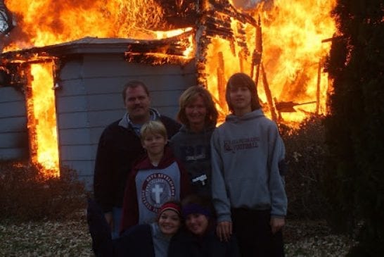 family posing in front of burning house